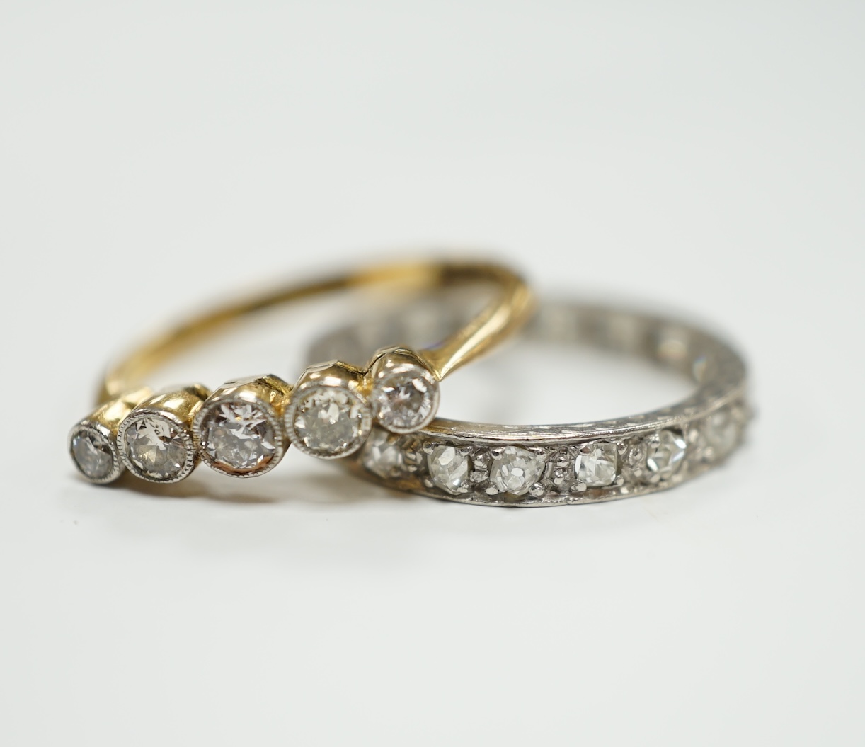 A white metal and diamond chip set full eternity ring, size L and an 18ct and graduated five stone diamond set ring, size M.